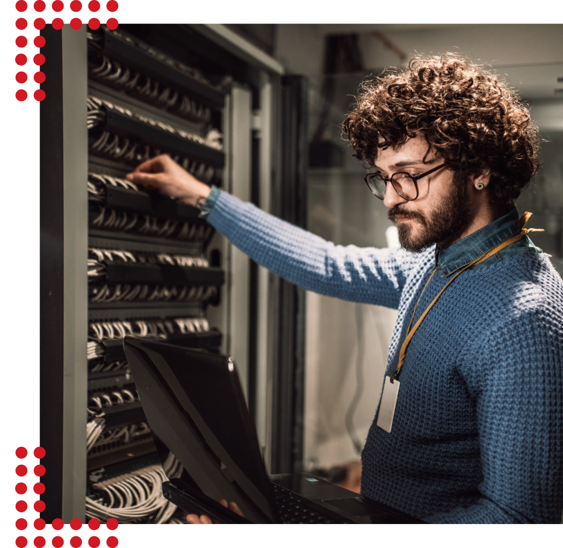 Ein junger sympathischer Mann mit wilden Locken und einem leichten Lächeln steht in einem Serverraum und richtet sorgfältig alles ein