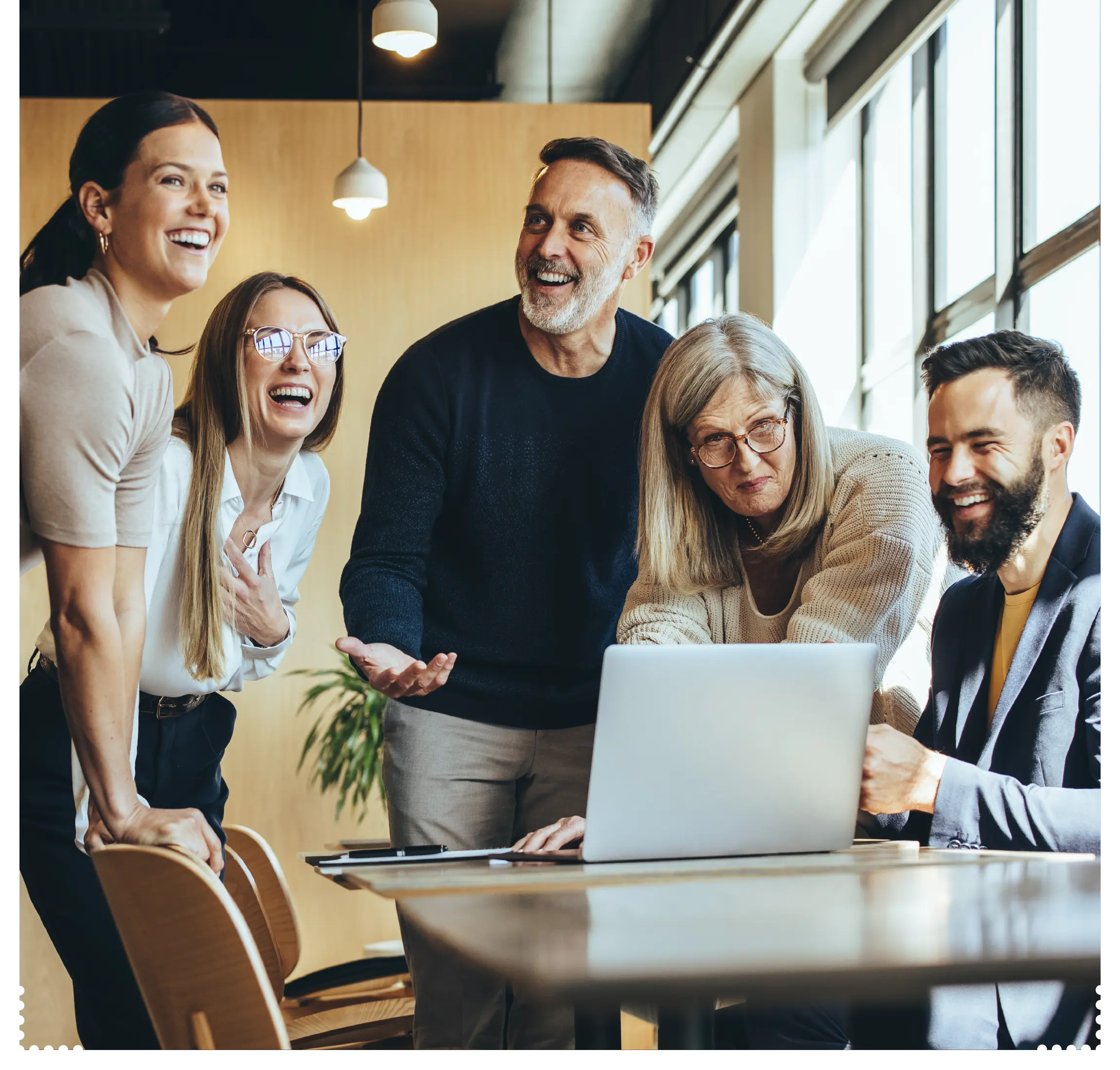 Eine toll gemischte Gruppe an Menschen sitzen um einen Laptop und arbeiten gemeinsam in einem modernen Arbeitsumfeld